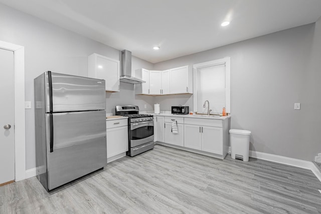 kitchen featuring stainless steel appliances, sink, white cabinets, light wood-type flooring, and wall chimney range hood