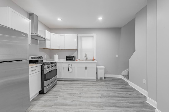 kitchen with stainless steel appliances, sink, white cabinetry, light hardwood / wood-style flooring, and wall chimney range hood