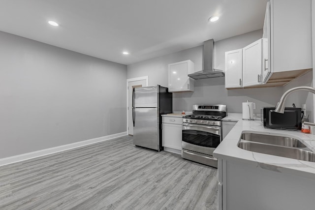 kitchen featuring white cabinets, appliances with stainless steel finishes, wall chimney range hood, and sink