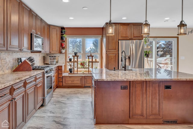 kitchen featuring light stone countertops, hanging light fixtures, a center island with sink, plenty of natural light, and appliances with stainless steel finishes