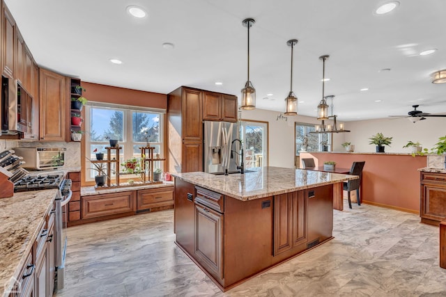 kitchen featuring light stone countertops, decorative light fixtures, an island with sink, appliances with stainless steel finishes, and ceiling fan