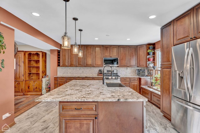 kitchen with a kitchen island with sink, appliances with stainless steel finishes, light stone countertops, pendant lighting, and sink