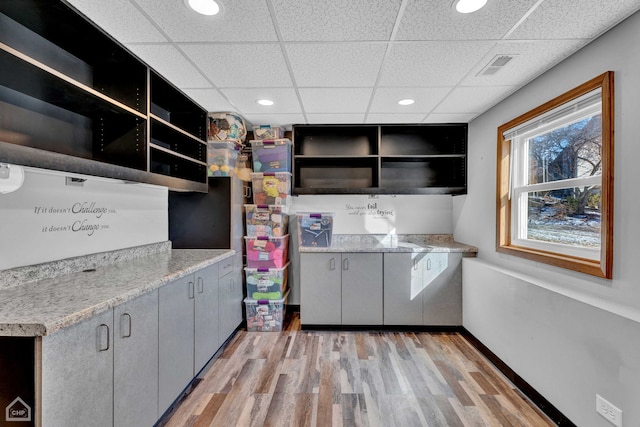 kitchen with a paneled ceiling, light hardwood / wood-style floors, light stone counters, and gray cabinets