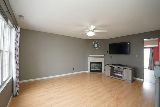 unfurnished living room with a tiled fireplace, ceiling fan, and light hardwood / wood-style flooring