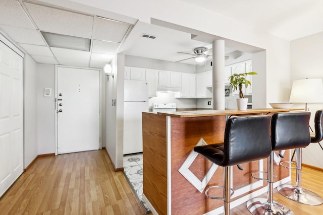 kitchen featuring kitchen peninsula, a paneled ceiling, white cabinetry, light hardwood / wood-style floors, and white fridge