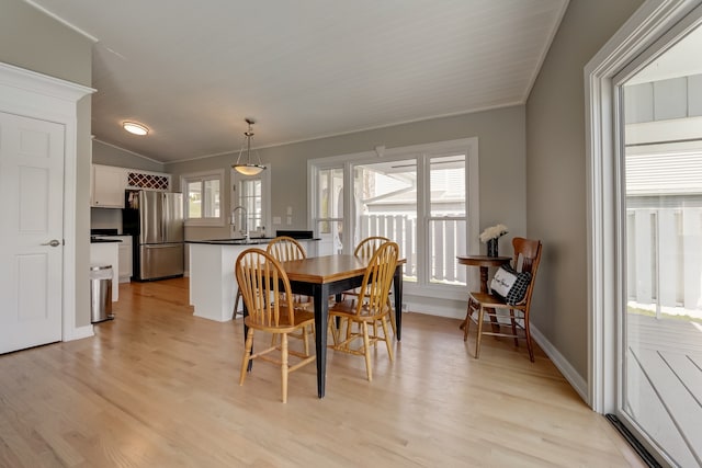 dining space with ornamental molding, vaulted ceiling, and light hardwood / wood-style flooring