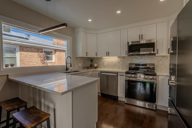 kitchen with stainless steel appliances, sink, kitchen peninsula, a breakfast bar area, and pendant lighting