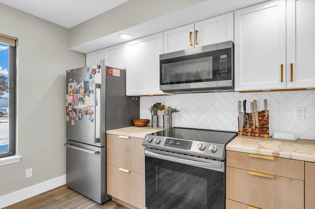 kitchen featuring light stone countertops, white cabinets, appliances with stainless steel finishes, light hardwood / wood-style floors, and backsplash