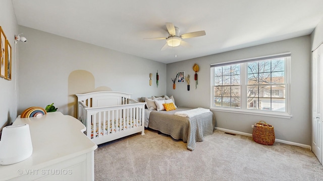 bedroom featuring ceiling fan, light colored carpet, and a nursery area