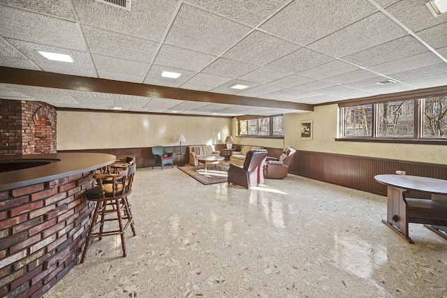 living room featuring bar area, a drop ceiling, and wooden walls