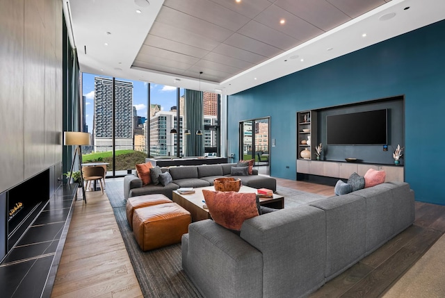 living room with a tray ceiling, a large fireplace, expansive windows, and hardwood / wood-style flooring