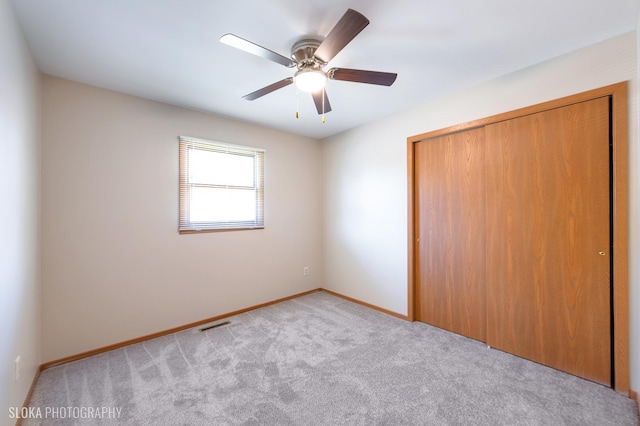 unfurnished bedroom featuring ceiling fan, light colored carpet, and a closet