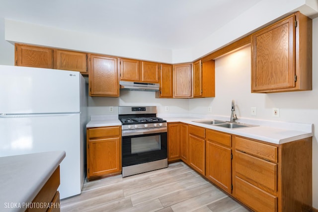 kitchen with white refrigerator, stainless steel gas stove, sink, and light hardwood / wood-style floors