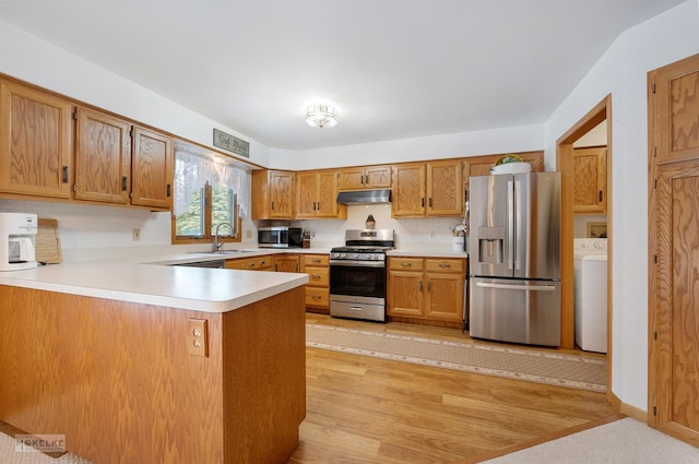 kitchen with kitchen peninsula, stainless steel appliances, light hardwood / wood-style flooring, washer / clothes dryer, and sink