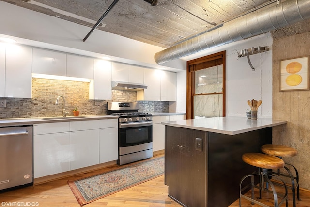 kitchen with under cabinet range hood, a sink, a kitchen breakfast bar, white cabinets, and appliances with stainless steel finishes