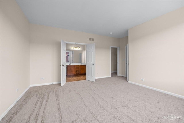 unfurnished bedroom featuring connected bathroom and light carpet