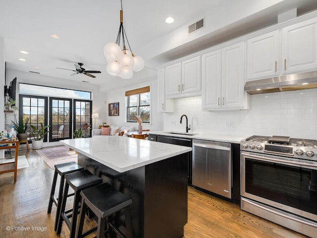 kitchen featuring stainless steel appliances, white cabinets, decorative light fixtures, a center island, and sink