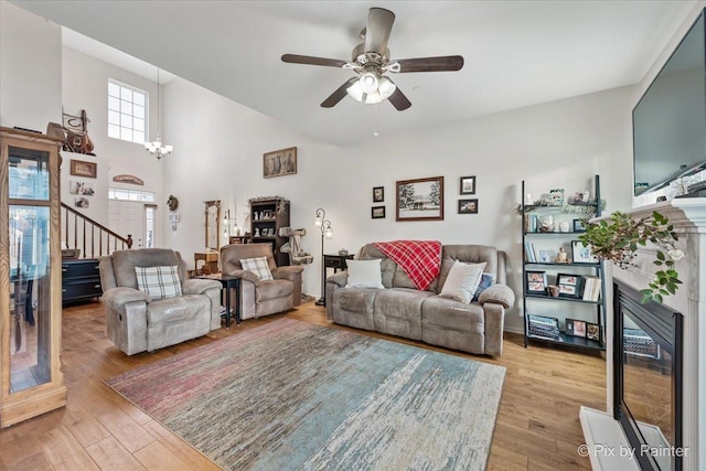 living room with light wood-type flooring, a towering ceiling, and ceiling fan with notable chandelier