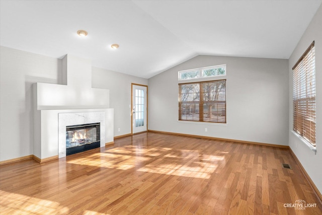 unfurnished living room featuring wood-type flooring, a high end fireplace, and vaulted ceiling