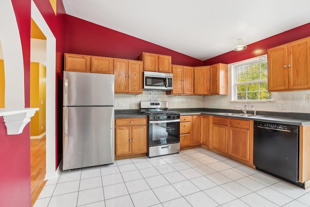 kitchen with stainless steel appliances, sink, lofted ceiling, light tile patterned floors, and backsplash