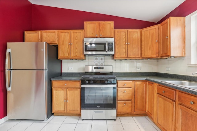 kitchen with sink, vaulted ceiling, light tile patterned flooring, tasteful backsplash, and appliances with stainless steel finishes