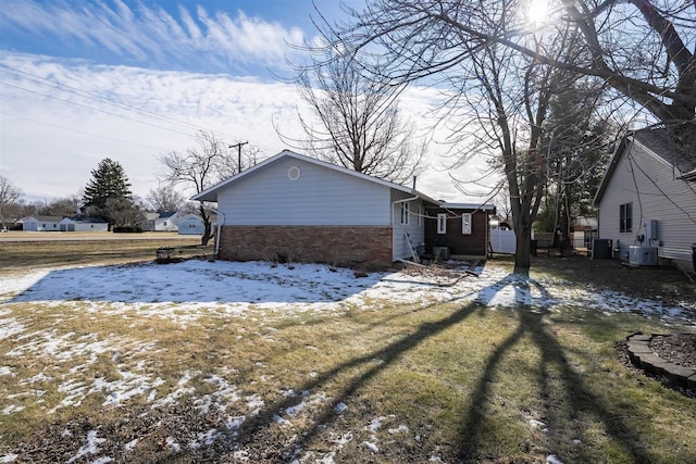 snow covered back of property with central AC unit and a yard