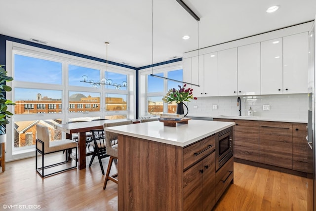 kitchen with sink, decorative light fixtures, stainless steel microwave, light hardwood / wood-style floors, and white cabinets