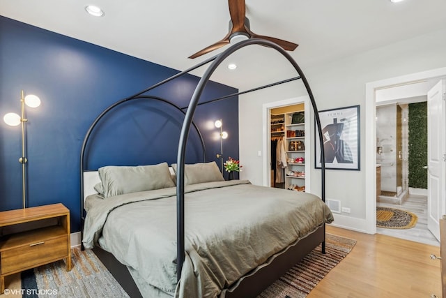 bedroom featuring light wood-type flooring, a spacious closet, ceiling fan, ensuite bath, and a closet