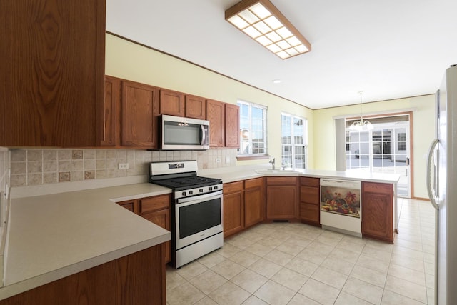 kitchen with an inviting chandelier, kitchen peninsula, stainless steel appliances, decorative backsplash, and pendant lighting