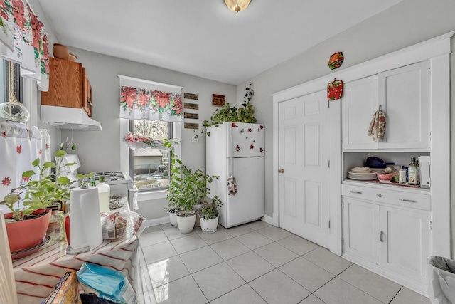 kitchen with white fridge, light tile patterned flooring, and white cabinetry