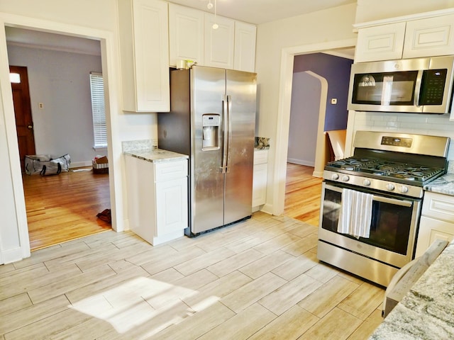 kitchen with stainless steel appliances, white cabinetry, and light stone countertops