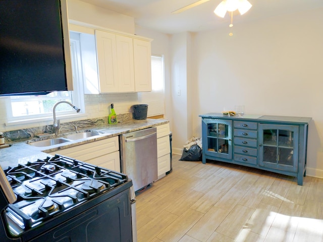 kitchen featuring light wood finished floors, tasteful backsplash, dishwasher, black range with gas stovetop, and a sink