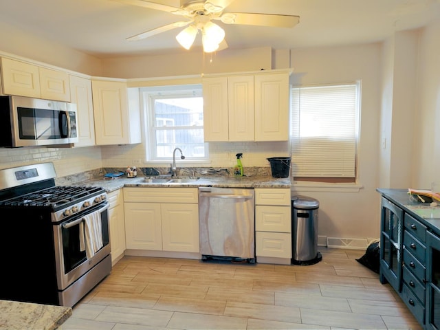 kitchen featuring wood finish floors, decorative backsplash, appliances with stainless steel finishes, a sink, and light stone countertops