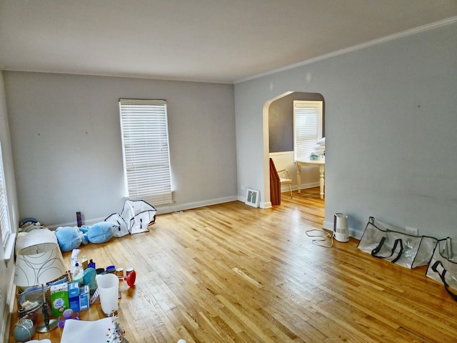 empty room featuring ornamental molding, arched walkways, baseboards, and wood finished floors