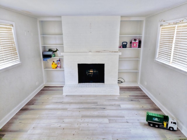 unfurnished living room featuring baseboards, a brick fireplace, wood finished floors, and built in features