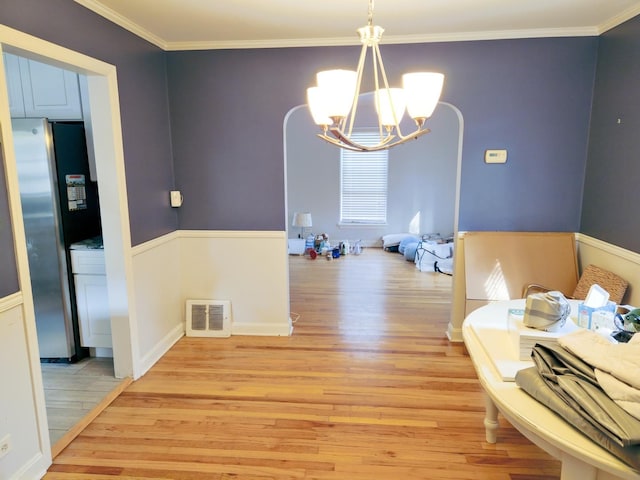 interior space featuring light wood finished floors, visible vents, arched walkways, and ornamental molding