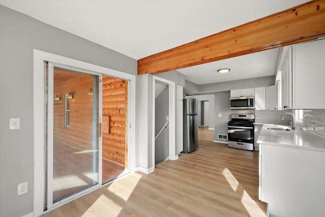 kitchen featuring light hardwood / wood-style flooring, stainless steel appliances, white cabinetry, beamed ceiling, and sink