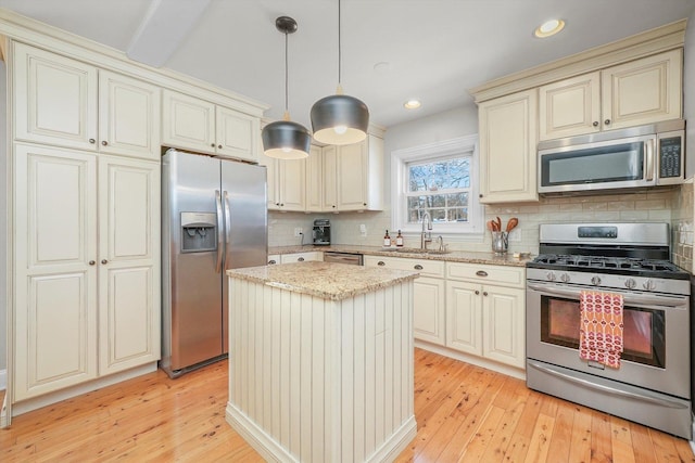 kitchen with cream cabinetry, stainless steel appliances, hanging light fixtures, a kitchen island, and sink