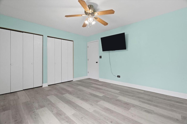 unfurnished bedroom featuring two closets, light hardwood / wood-style floors, and ceiling fan