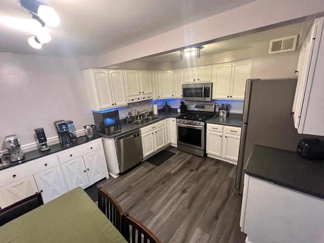 kitchen featuring sink, stainless steel appliances, white cabinetry, and dark hardwood / wood-style flooring