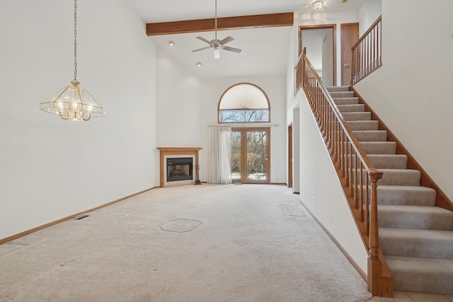 unfurnished living room featuring light carpet, ceiling fan with notable chandelier, beam ceiling, and a high ceiling