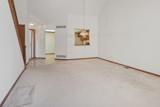 empty room with high vaulted ceiling, light colored carpet, and an inviting chandelier