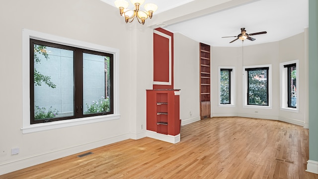 unfurnished living room with a healthy amount of sunlight, ceiling fan with notable chandelier, and light wood-type flooring