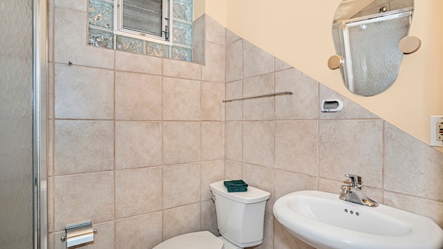 bathroom with walk in shower, toilet, sink, and tile walls