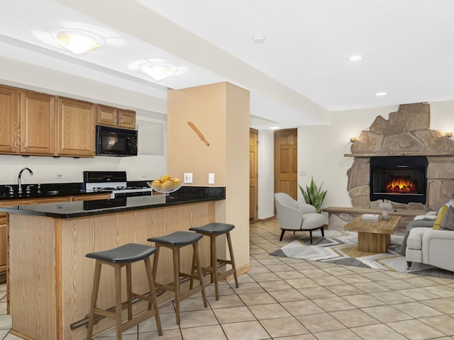 kitchen featuring a breakfast bar, a fireplace, sink, white gas range oven, and kitchen peninsula