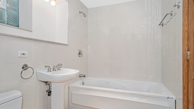 full bathroom featuring toilet, tiled shower / bath combo, sink, and tile walls