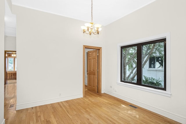 spare room with crown molding, an inviting chandelier, and light wood-type flooring