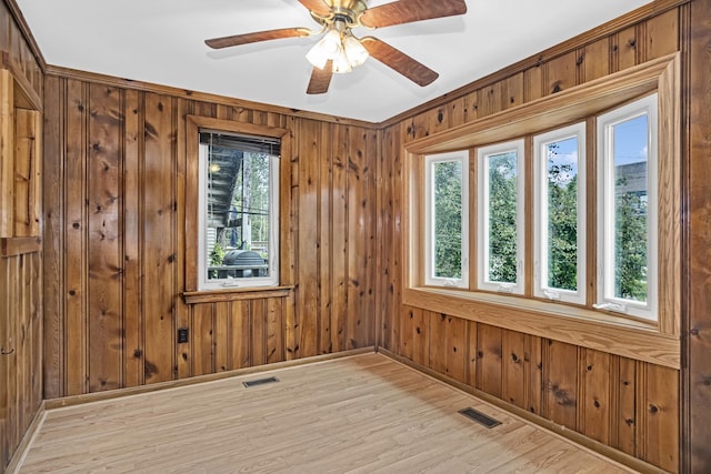 spare room with plenty of natural light, wood walls, ceiling fan, and light wood-type flooring
