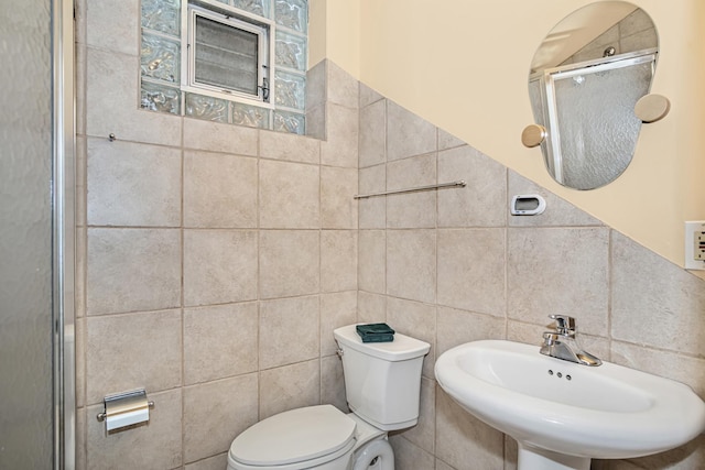 bathroom featuring walk in shower, toilet, sink, and tile walls