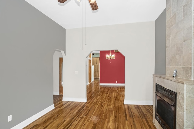 unfurnished living room with wood-type flooring, a fireplace, and ceiling fan with notable chandelier